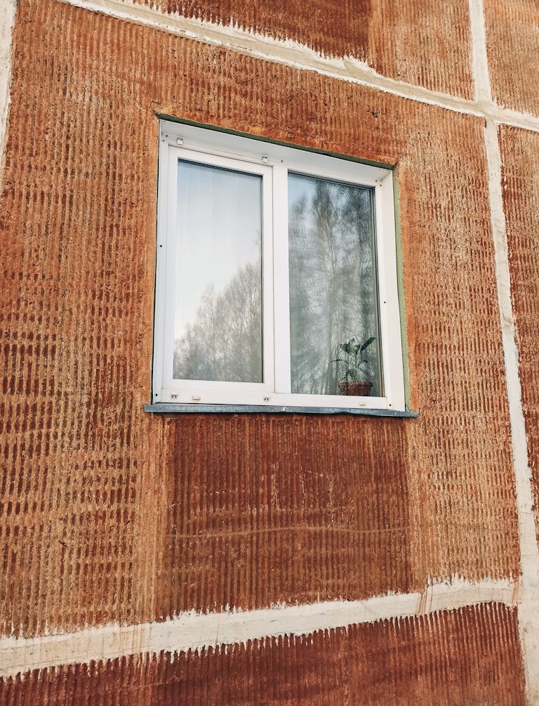 Close-up of a textured brown wall with a window featuring reflections and a potted plant.