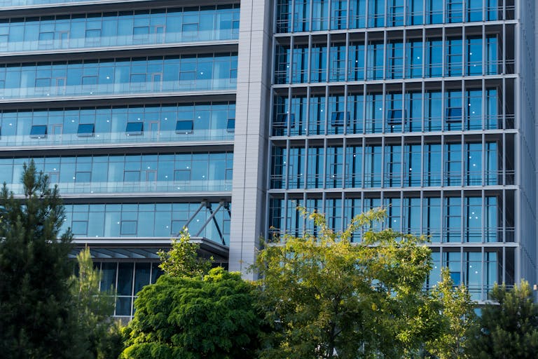 Contemporary high-rise office building with blue glass facade reflecting the sky and surrounding trees.