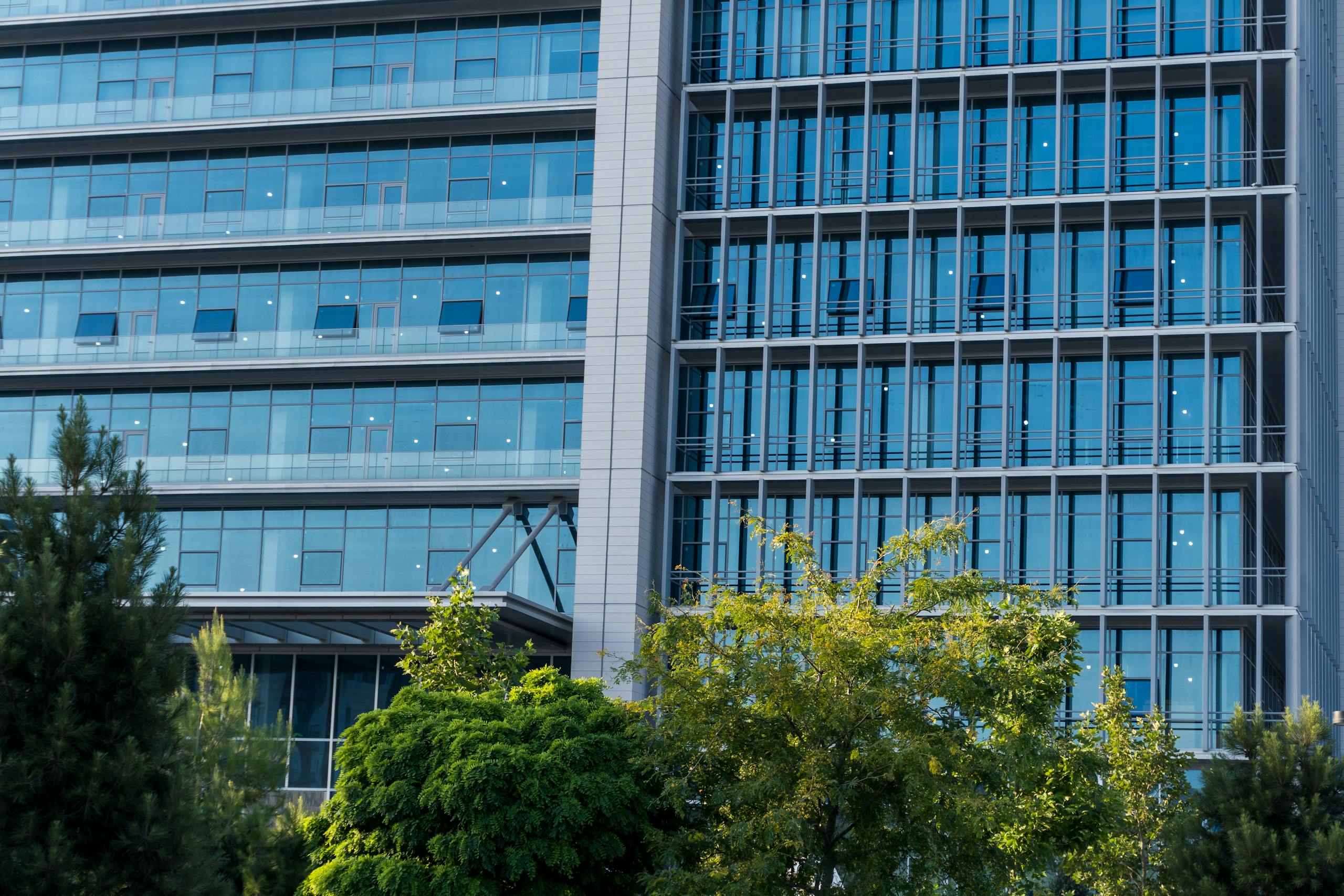 Contemporary high-rise office building with blue glass facade reflecting the sky and surrounding trees.