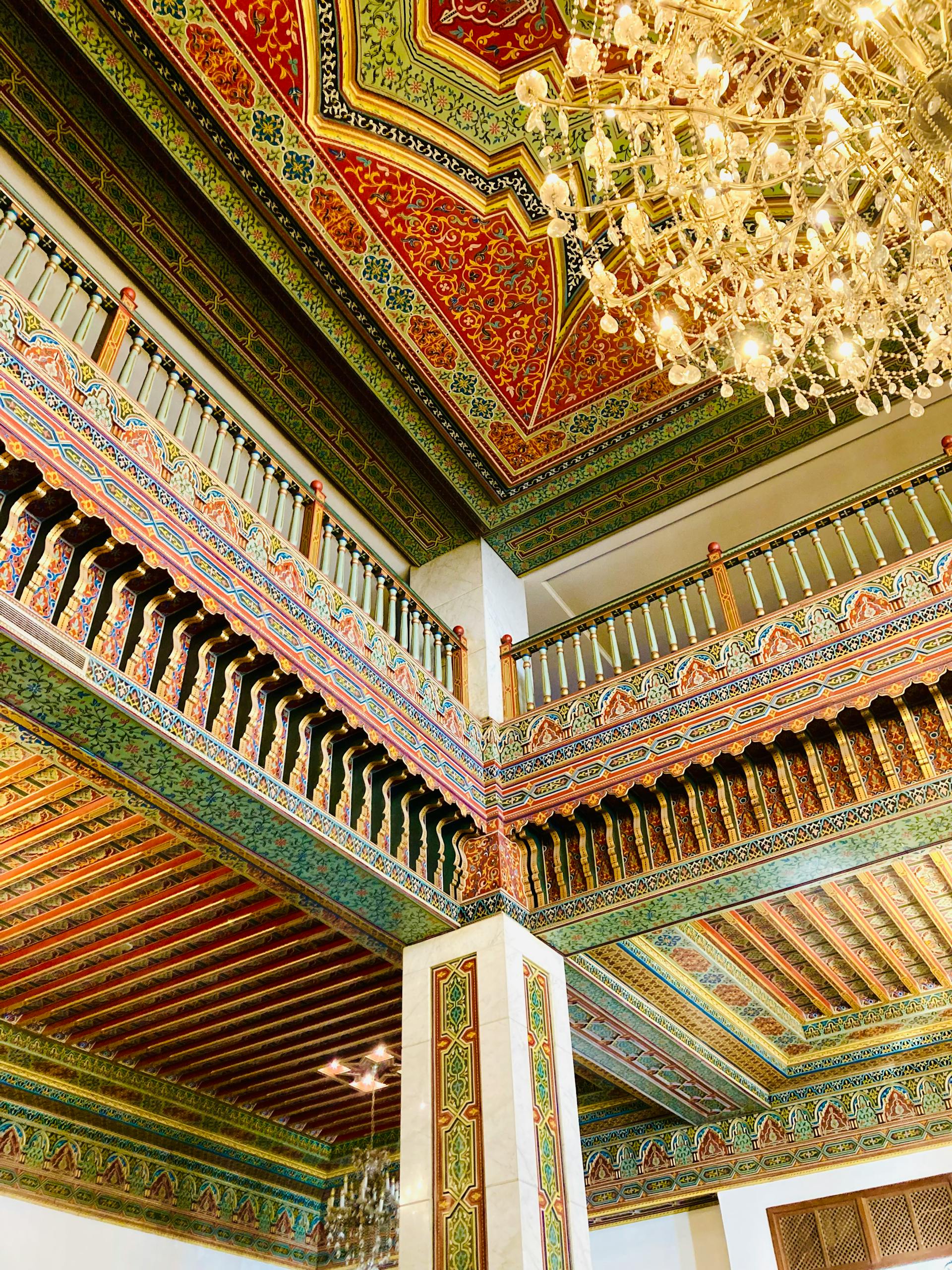 Detailed view of an ornate indoor balcony and ceiling with intricate designs and chandelier.