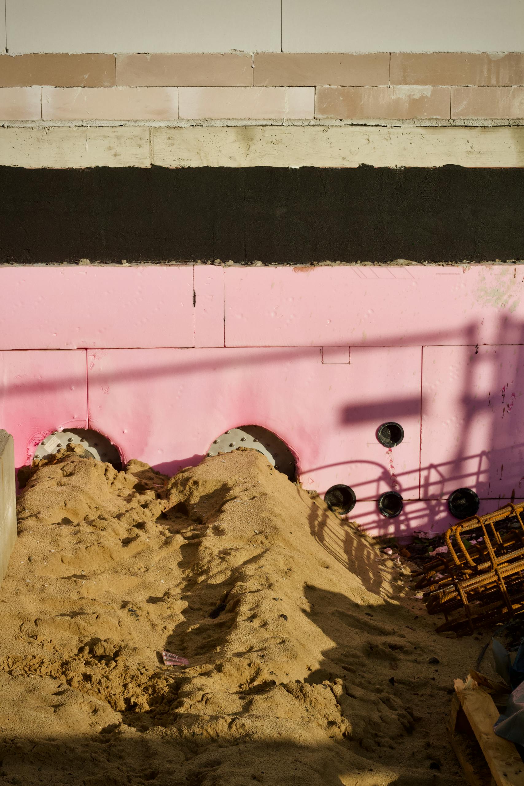Image of a construction site featuring pink insulation panels against a sandy foreground.